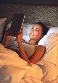Some bedtime browsing. a young woman watching movies on her tablet in bed