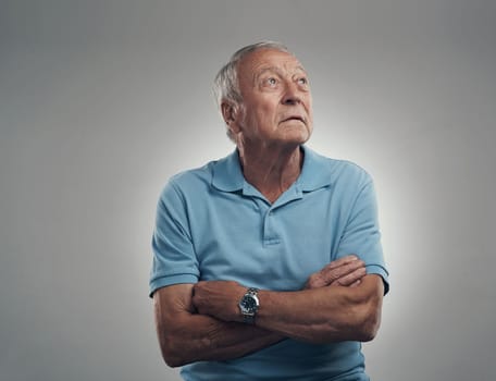 What is that light over there. an older man with his arms crossed looking off into the distance in a studio against a grey background
