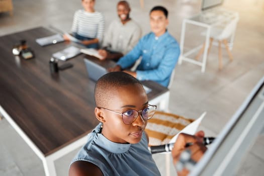 Group of diverse businesspeople having a meeting in an office at work. Young african american businesswoman writing an idea on a whiteboard in a boardroom with colleagues. Businesspeople planning tog.