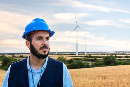 Pensive electric engineer standing at wind turbine farm. Copy space. Renewable energy concept.