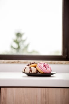 Plate with donuts next to window sill. Delicious junck food