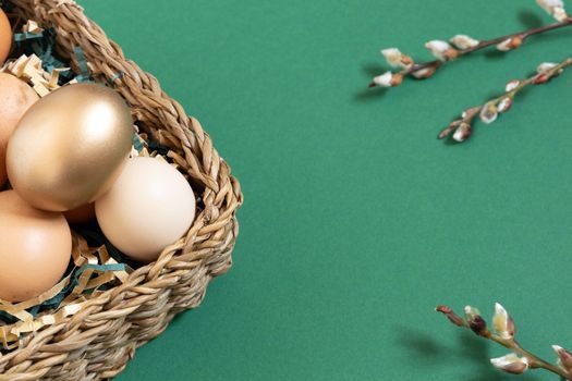 Easter eggs natural and gold in basket with paper filler . Branch of willow catkins. Light pastel orange background with copy space.