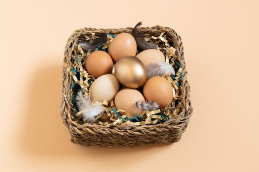 Easter eggs natural and gold in basket with feather. Branch of willow catkins. Light pastel orange background with copy space.