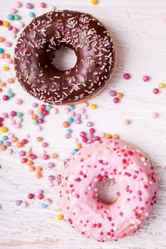 Overtop view of donuts in and sweet candy on white wooden background. Delicious junk food