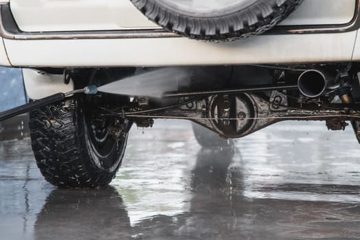 Washing the rear suspension of an SUV with a high-pressure water jet at a self-service car wash.