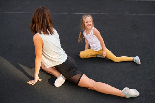 Mother and daughter go in for sports outdoors. Caucasian woman and little girl are engaged in fitness at the stadium