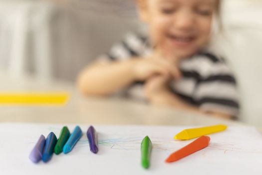 Selective focus on colorful crayons. Happy caucasian baby girl sitting at the table at home drawing abstract picture. Early development, precocity concept