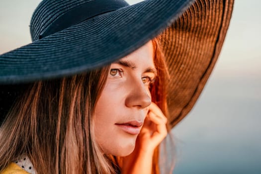 Portrait of happy young woman wearing summer black hat with large brim at beach on sunset. Closeup face of attractive girl with black straw hat. Happy young woman smiling and looking at camera at sea