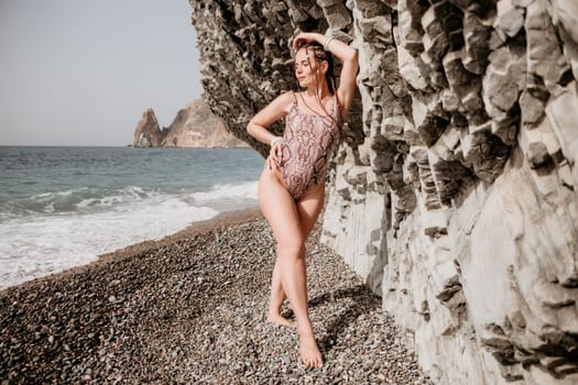 Beach vacation. Hot beautiful woman in sunhat and bikini standing with her arms raised to her head enjoying looking view of beach ocean on hot summer day.