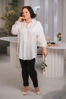 An adult woman in a white shirt holds one rose in her hands while standing in the interior. Pink roses.