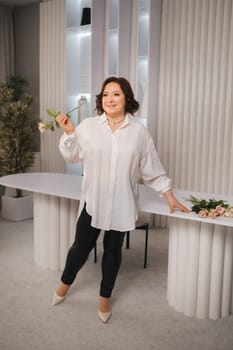 An adult woman in a white shirt holds one rose in her hands while standing in the interior. Pink roses.