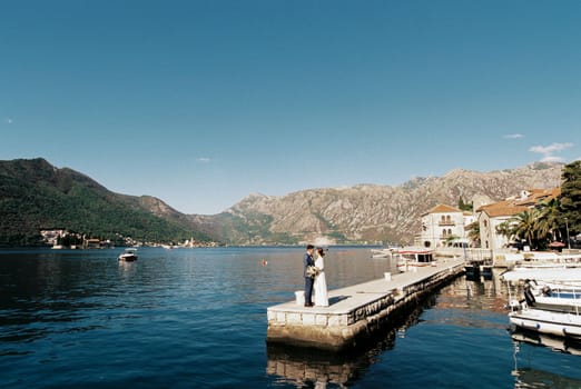 Groom holds bride hands on the pier by the sea against the backdrop of old houses. High quality photo