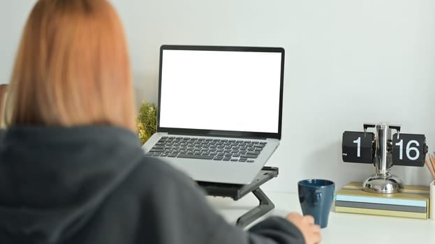 Back view of creative female freelancer sitting in comfortable workplace and working online with laptop computer.