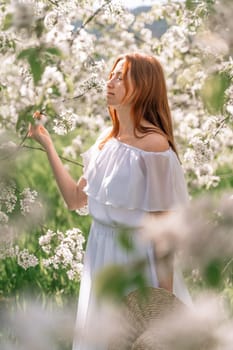 Woman cherry orchard. A happy woman in a long white long dress walks through the green spring blooming cherry garden. Happy cheerful princess bride. The fabric of the skirt flutters in the wind