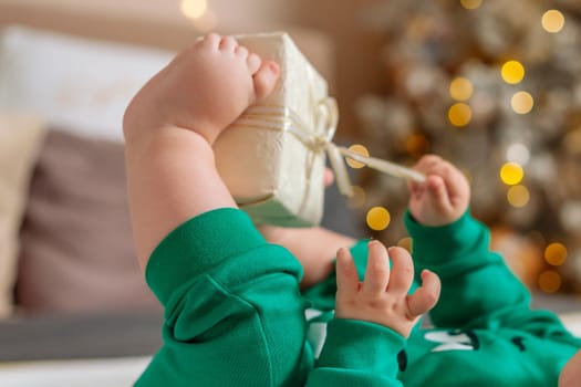 Kid gift. A little boy in a green suit holds a gift box with his feet and hands in bed