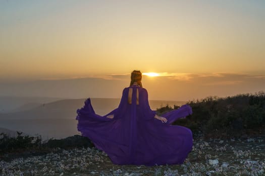 Sunset purple dress woman mountains. Rise of the mystic. sunset over the clouds with a girl in a long purple dress. In the meadow there is a grass dream with purple flowers