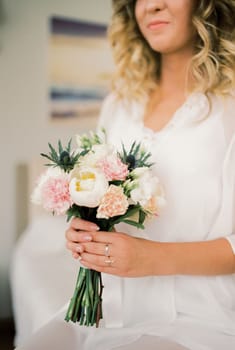 Bouquet of flowers in the hands of the bride in a white dressing gown. High quality photo