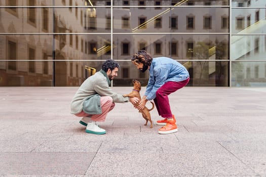 male couple playing with their playful little dog on the street, concept of family lifestyle with pets and love between people of the same sex, copy space for text
