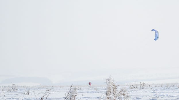 A girl in a red jumpsuit is kiting on skis in snowy winter terrain.