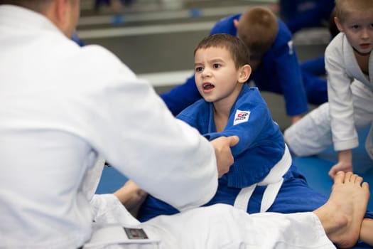 Belarus, city of Gomil, December 15, 2021. Judo school for children. The trainer stretches the child in kimano.