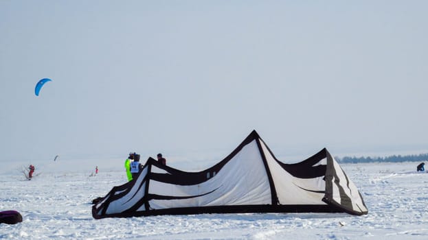 people kiting in winter in snowy terrain. snowkiting. tent.