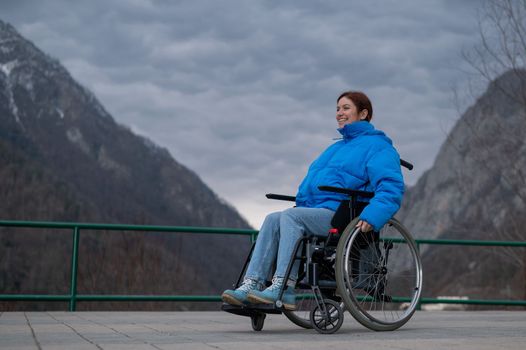 A woman in a wheelchair on a point view admires the high mountains. Thrust to life