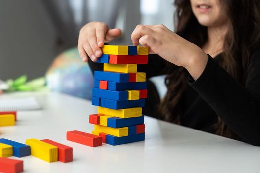 a little happy girl is playing the board game jenga at the table. Construction of a tower made of wooden cubes.