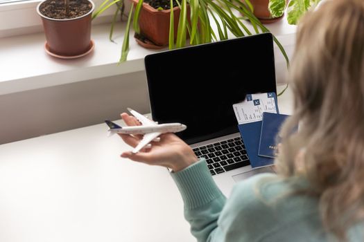Woman dreaming about travel while self isolation at home. Caucasian girl with toy airplane and laptop.