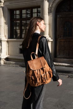 beautiful young girl with dark hair wearing jeans and a leather jacket posing outside with a leather backpack