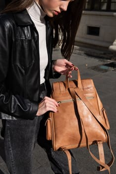 beautiful young girl with dark hair wearing jeans and a leather jacket posing outside with a leather backpack