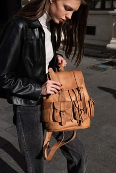 beautiful young girl with dark hair wearing jeans and a leather jacket posing outside with a leather backpack