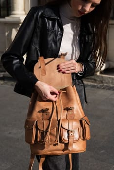beautiful young girl with dark hair wearing jeans and a leather jacket posing outside with a leather backpack