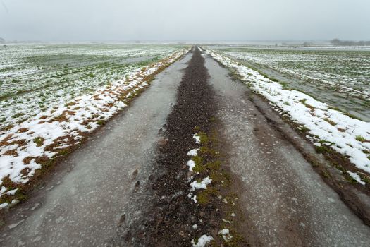 Icy dirt road through fields with snow and water, view on a foggy day, Czulczyce, Poland