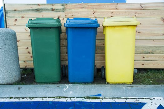 Green, blue and yellow waste bins standing in a row, front view