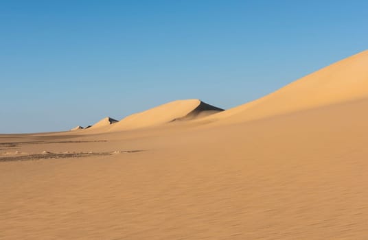 Landscape scenic view of desolate barren western desert in Egypt with Karaween large sand dunes against blue sky background