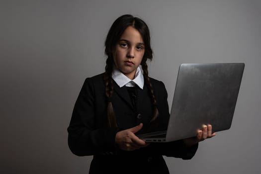 A girl with braids in a gothic style on a dark background with laptop.