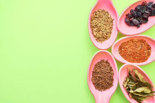 Pan aromatic or pungent vegetable substance used to flavor food, e.g. cloves, pepper, or cumin. Pink spoons with spices for cooking on a green surface.