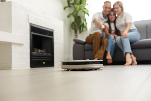 Young family resting on the couch while robotic vacuum cleaner doing its work at home. Household robots concept