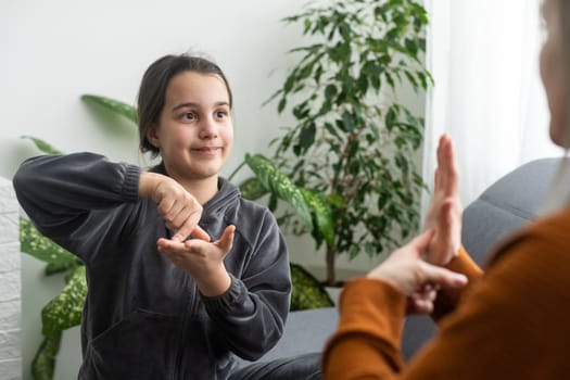 daughter talk with middle aged mother people using sign language, family sitting on armchair side view, teacher teach teenager deaf-mute girl to visual-manual gestures symbols concept image.