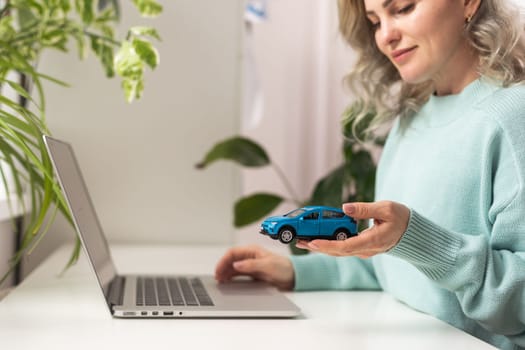 Sales woman is recording document on a laptop with car models and notebooks on the desk, concept of selling contracts