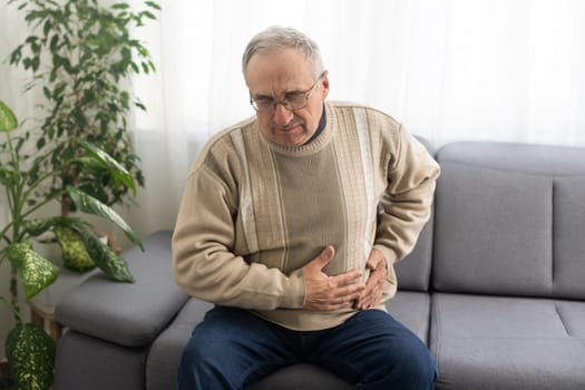Elderly men have abdominal pain sitting on the sofa in the house. Concept Problems of the digestive tract in older people, health care