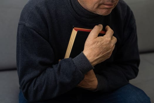 Senior man praying, holding Bible.