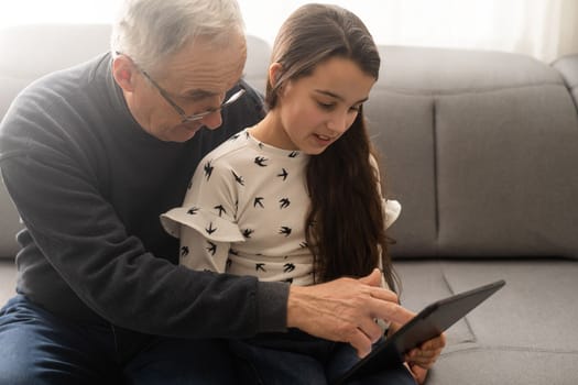 Senior man with his grandchild looking together on photos in tablet.