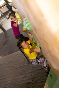 Young female bouldering instructor helping boy climb artificial wall.