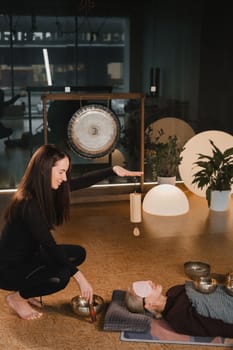 A young beautiful woman is doing a massage with singing bowls and a koshi bell to another girl. Sound therapy.