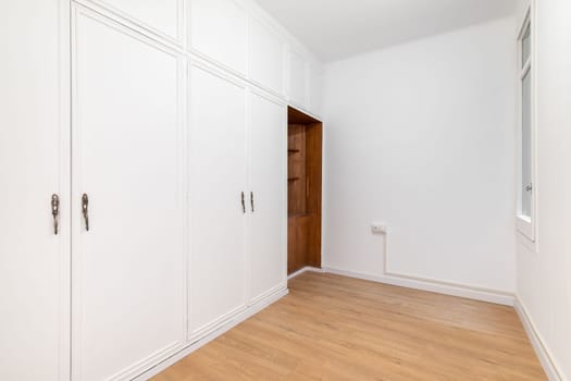 Built-in spacious wardrobes in a room with wooden laminate flooring. Concept of organizing storage and laconic interior.