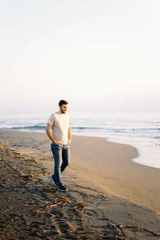 Young man in jeans walking along the sandy beach near the water. High quality photo