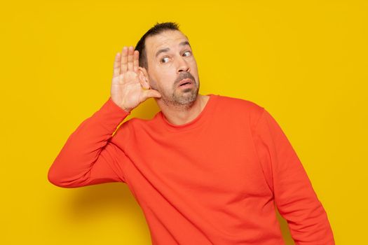 Listening Hispanic man holds his hand near his ear on a yellow background. Handsome man trying to listen to someone's conversation.