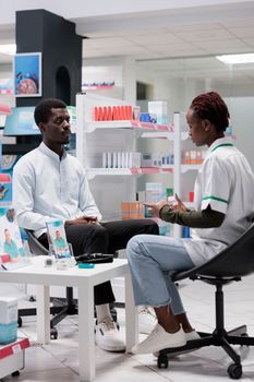 Pharmacist consultation, drugstore seller advising medicaments, holding pills package. African american man and medic talking, chemist and client communication, all black team