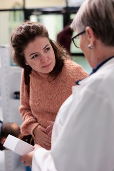 Young adult customer holding hands on belly suffering from painful abdominal cramps asking pharmacist for stomachache medicatio in pharmacy. Drugstore worker offering gastritis painkiller.